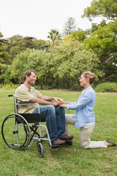Homem feliz em cadeira de rodas com o parceiro ajoelhado ao lado dele — Fotografia de Stock