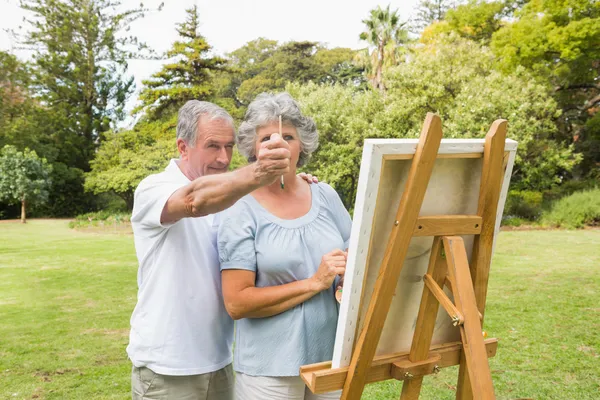 Content retired woman painting on canvas with husband — Stock Photo, Image