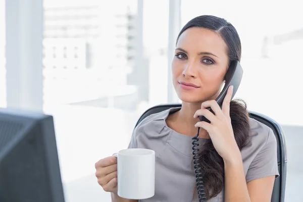 Serious secretary answering phone and drinking coffee — Stock Photo, Image