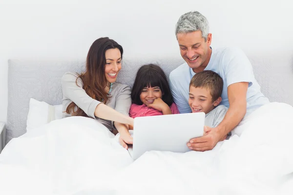 Família sorrindo deitada na cama usando seu laptop — Fotografia de Stock