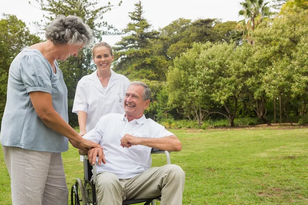 Homem feliz em uma cadeira de rodas rindo com sua enfermeira e esposa — Fotografia de Stock