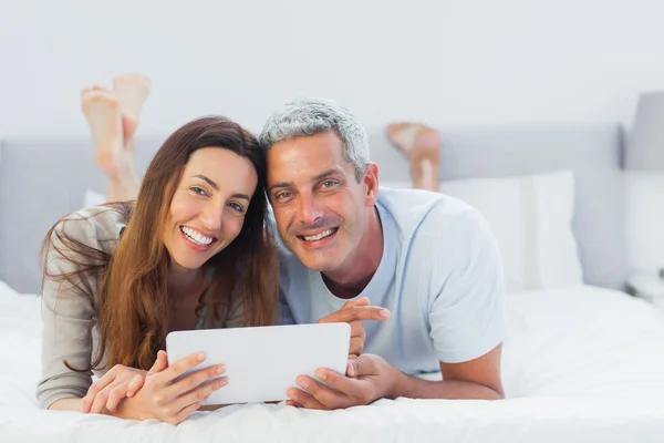 Fröhliches Paar liegt mit Tablet-PC im Bett — Stockfoto