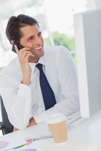 Lachende zakenman aan de telefoon kijken naar zijn computer — Stockfoto