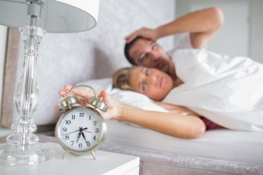 Tired couple looking at alarm clock in the morning with woman tu clipart