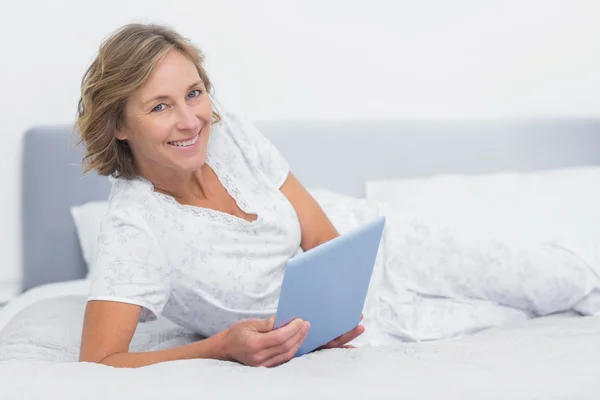Fröhliche blonde Frau liegt mit Tablet-PC im Bett — Stockfoto