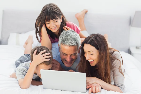 Famille souriante couchée sur le lit en utilisant leur ordinateur portable — Photo