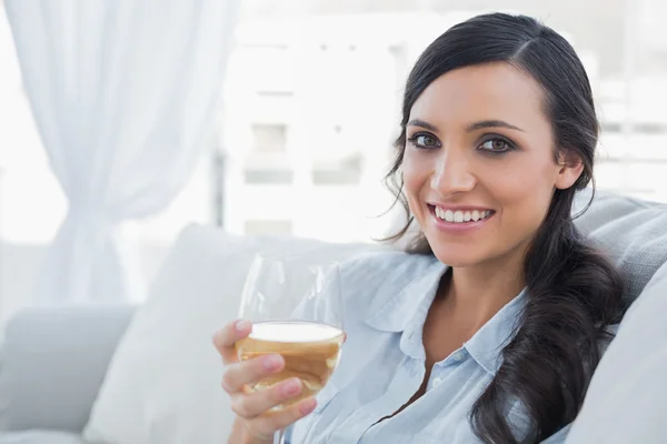 Gelukkig mooie brunette drinken van witte wijn zittend op de Bank — Stockfoto