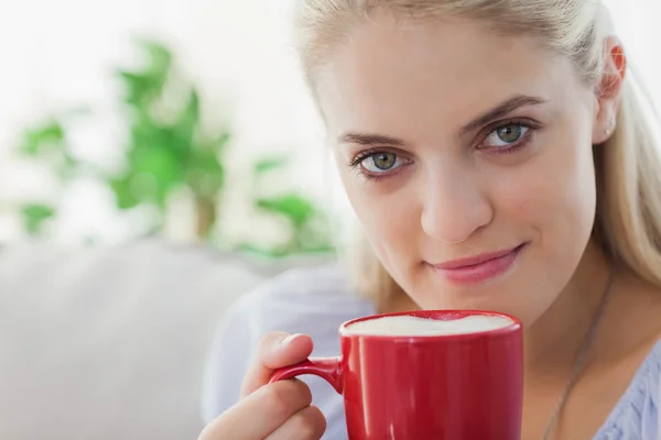 Mujer rubia sosteniendo una taza roja y sonriendo a la cámara — Foto de Stock