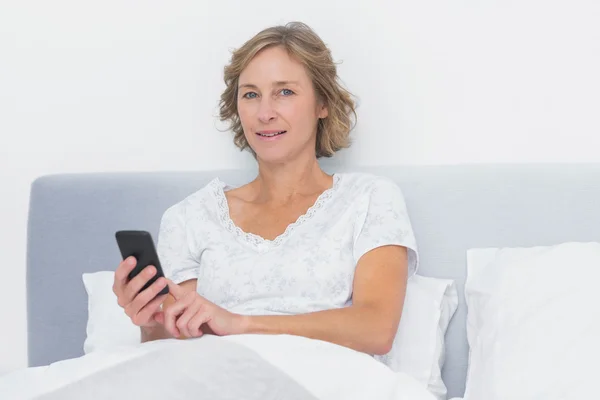 Glada blonda kvinnan skicka textmeddelande i sängen — Stockfoto