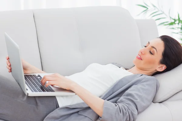 Smiling businesswoman lying on sofa using laptop — Stock Photo, Image