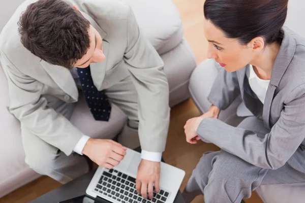 Coworkers parlando e utilizzando il computer portatile seduto sul divano — Foto Stock