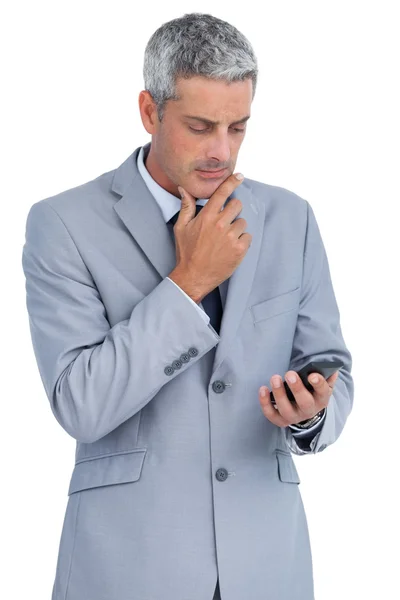 Задумчивый бизнесмен трогает подбородок и смотрит на свой телефон. — стоковое фото