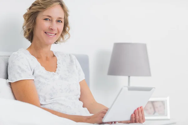 Mujer rubia alegre sentada en la cama usando tableta pc — Foto de Stock