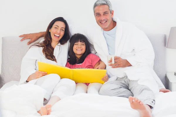 Parents with their daughter on bed looking together at photograp — Stock Photo, Image