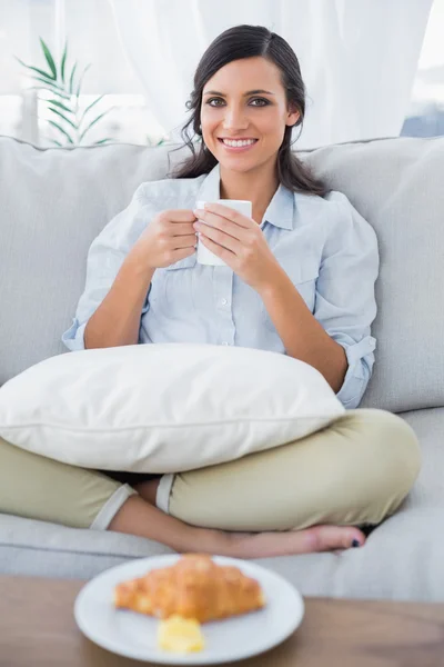 Mulher alegre no sofá beber café e ter croissant — Fotografia de Stock