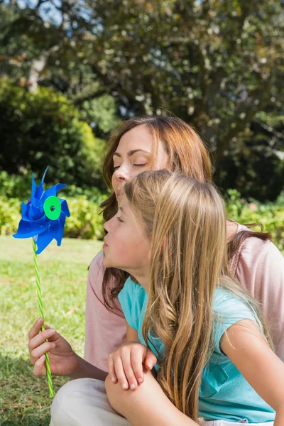 Mother with daughter blowing pinwheel in the park — Stock Photo, Image