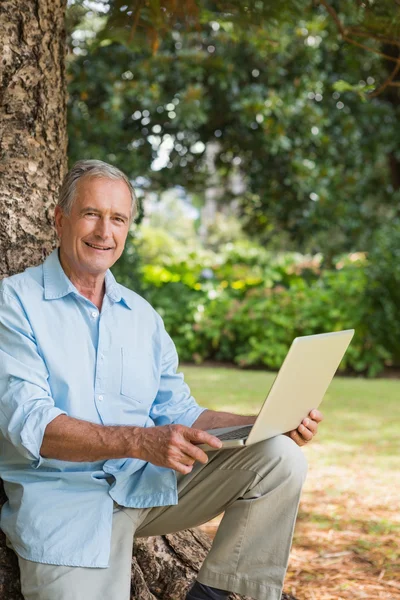 Oude man leunend tegen boom met een laptop — Stockfoto