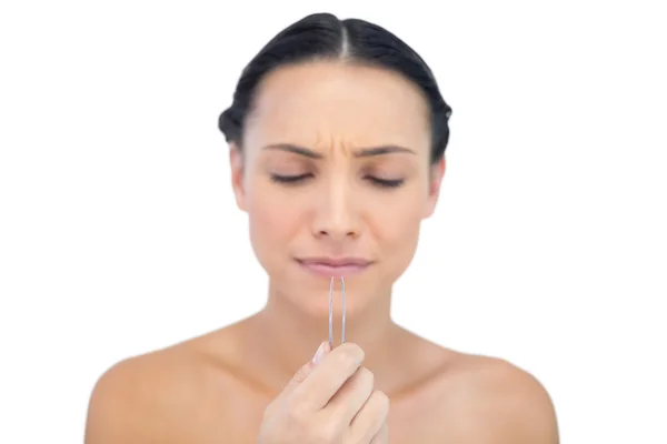 Young brunette looking at tweezers in her hand — Stock Photo, Image