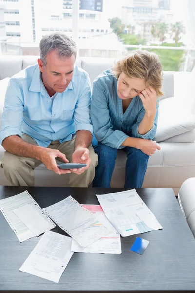 Middle aged couple sitting on their couch paying their bills — Stock Photo, Image