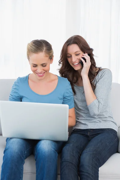 Blond woman using her laptop with her friend having a phone call — Stock Photo, Image