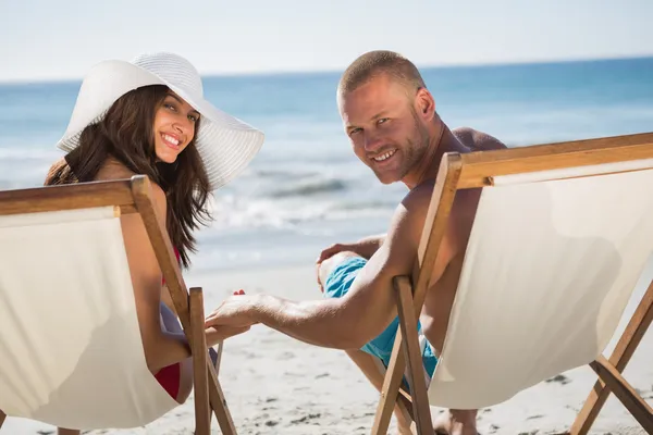 Cute couple looking at camera while lying on their deck chairs — Stock Photo, Image