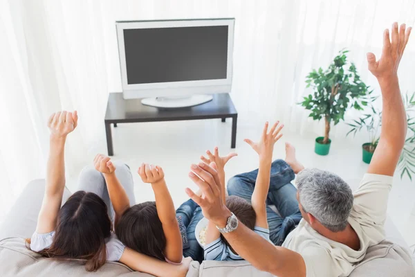 Family raising their arms in front of television — Stock Photo, Image