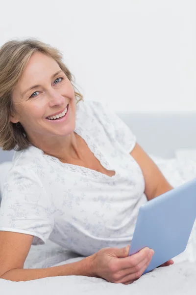 Mujer rubia sonriente acostada en la cama usando tableta pc — Foto de Stock