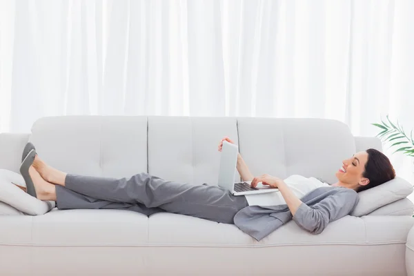 Businesswoman lying on sofa using her laptop — Stock Photo, Image