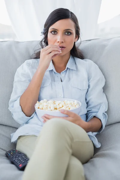 Jolie brune concentrée regardant la télévision et mangeant du maïs pop — Photo