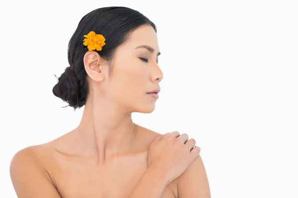 Pensive model with orange flower in hair touching her shoulder — Stock Photo, Image