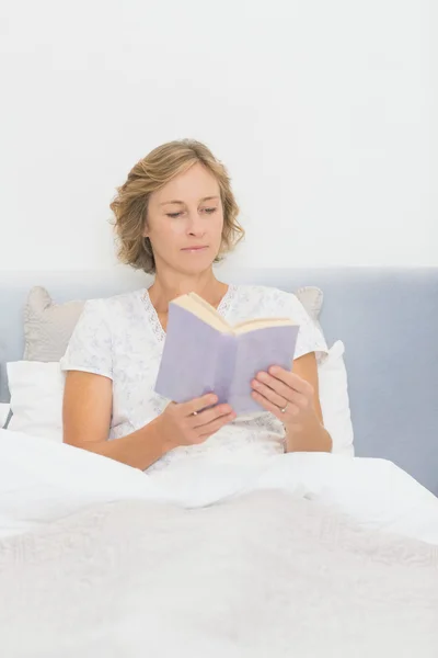 Blond kobieta siedzi w czytaniu łóżko — Zdjęcie stockowe