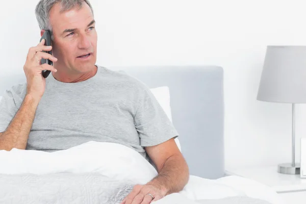Grey haired man making a phone call in bed — Stock Photo, Image