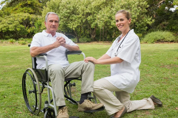 Glad man i en rullstol med hans sjuksköterska knä bredvid — Stockfoto