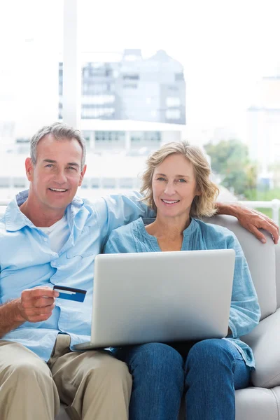 Casal alegre sentado em seu sofá usando o laptop — Fotografia de Stock