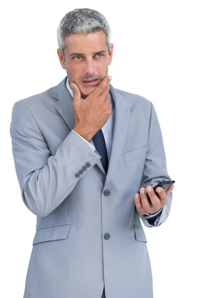 Homme d'affaires réfléchi touchant son menton tenant un téléphone portable — Photo