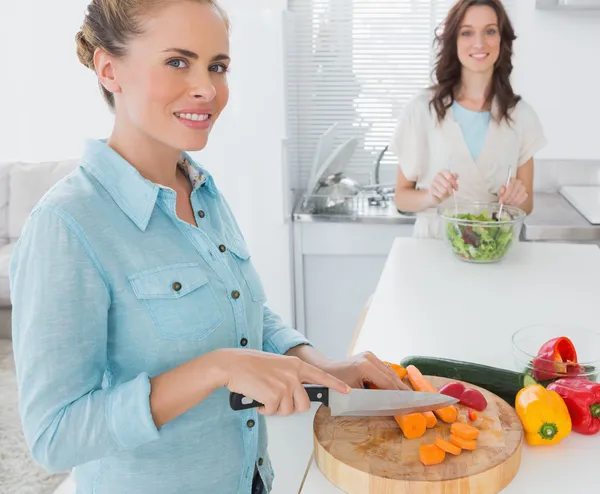 Mulher loira cortando cenouras com seu amigo jogando salada — Fotografia de Stock