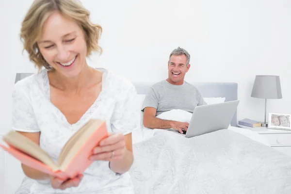 Mujer leyendo libro mientras marido está usando portátil —  Fotos de Stock