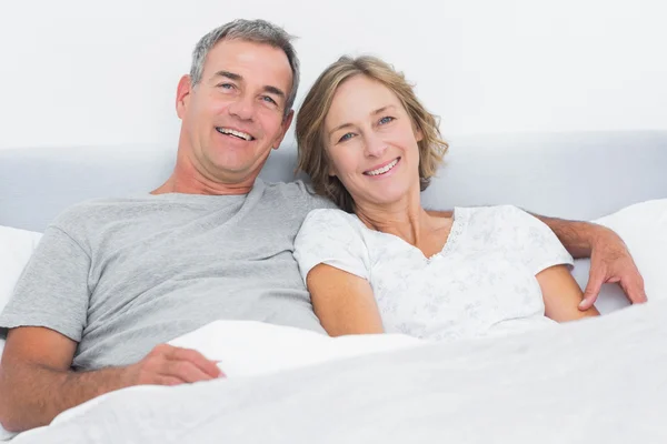 Glückliches Paar kuschelt im Bett und schaut in die Kamera — Stockfoto