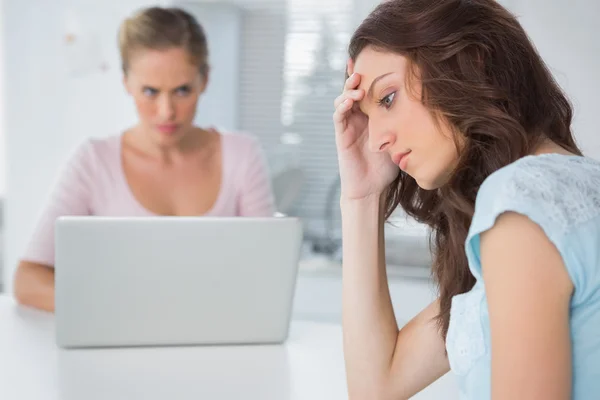 Forstyrret kvinde tænker, mens hendes vrede ven stirrer på hende - Stock-foto