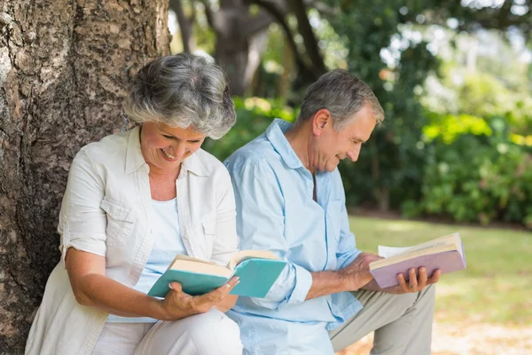 Retired couple reading books together sitting on tree trunk — Stock Photo, Image