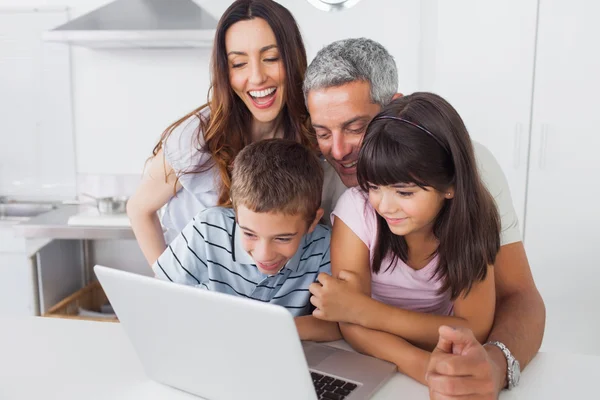 Sonriente familia sentada en la cocina usando su computadora portátil — Foto de Stock