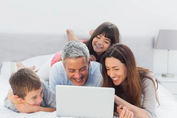 Rodina ležící na posteli pomocí jejich laptop — Stock fotografie