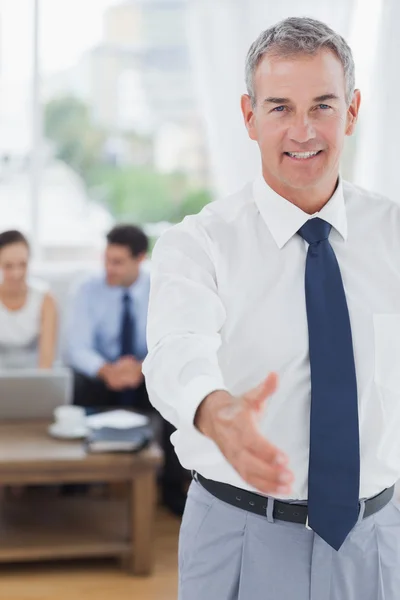 Executive standing on foreground holding out his hand — Stock Photo, Image