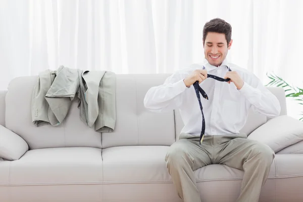 Lächelnder Geschäftsmann sitzt auf Sofa und löst seine Krawatte — Stockfoto