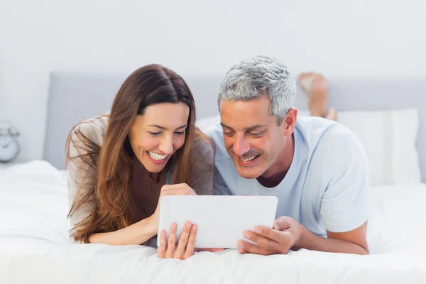 Casal deitado na cama usando seu tablet pc — Fotografia de Stock