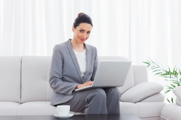 Smiling busineswoman sitting on sofa using laptop — Stock Photo, Image