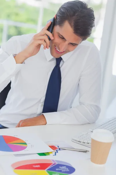Smiling businessman on the phone analyzing graphs — Stock Photo, Image