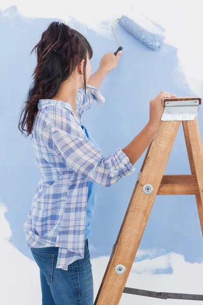 Woman using paint roller to paint wall blue — Stock Photo, Image