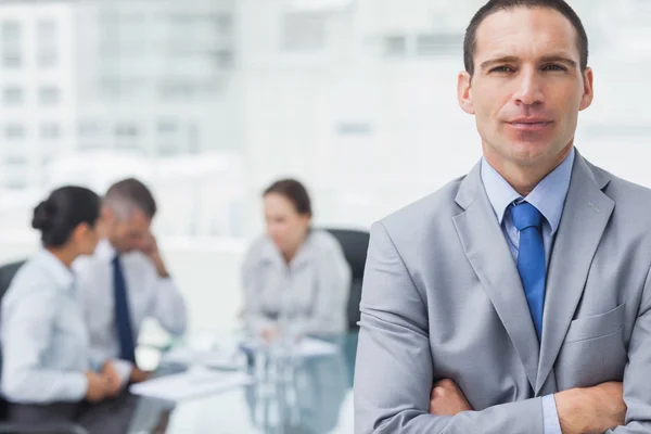 Hombre de negocios serio posando con compañeros de trabajo en segundo plano —  Fotos de Stock