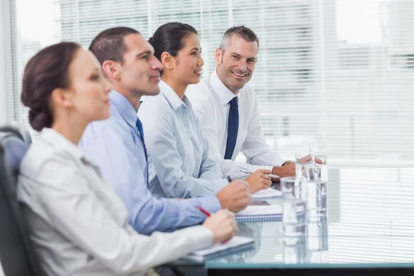 Empresario sonriendo a la cámara mientras sus colegas escuchan —  Fotos de Stock